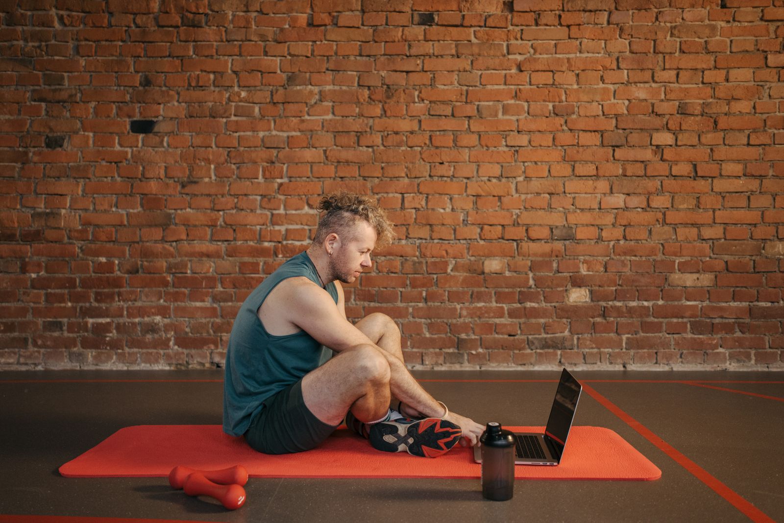 Fitness coach sitting on a gym mat checking a laptop